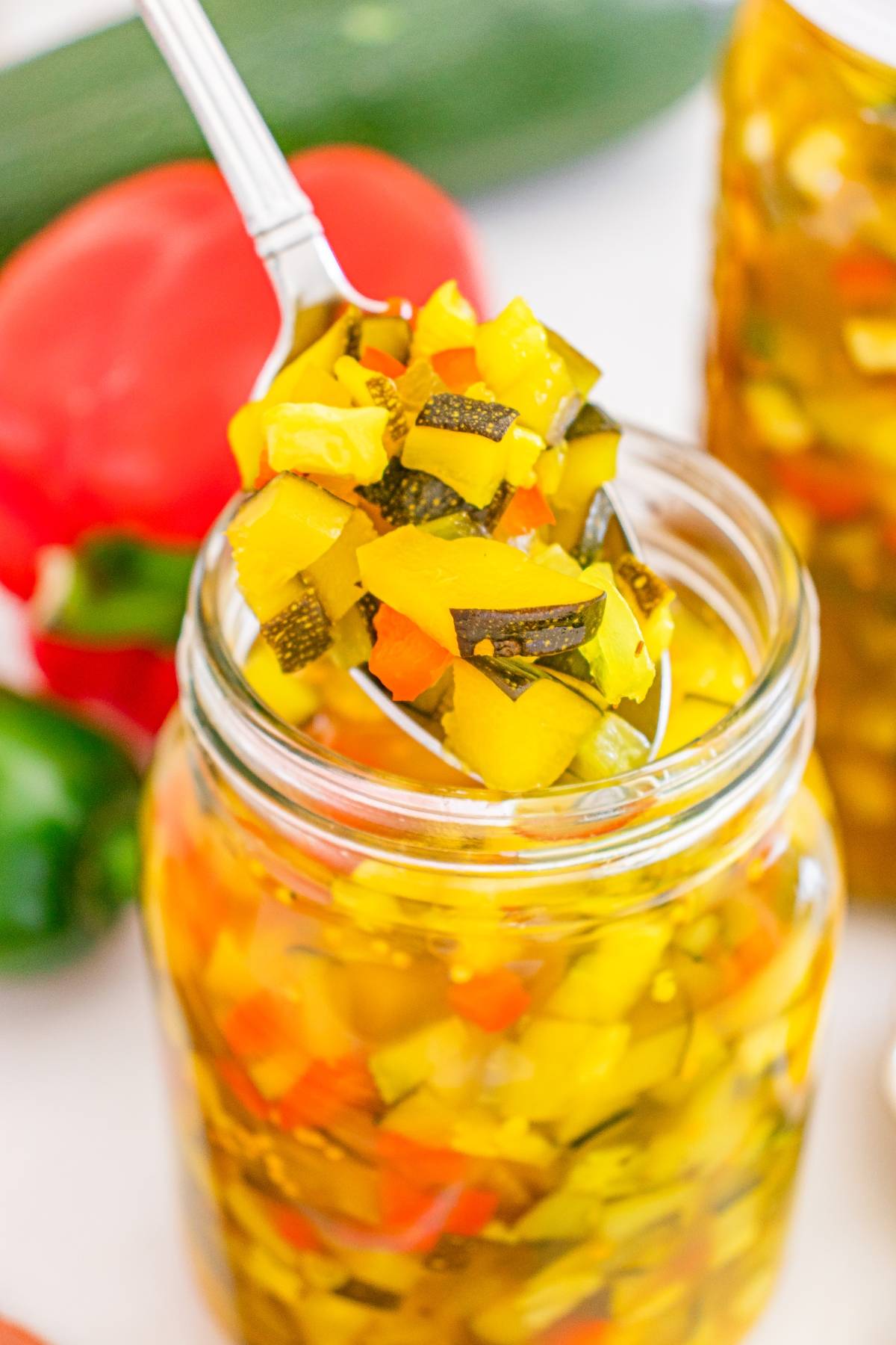 A spoonful of colorful pickled vegetables being lifted from a glass jar.