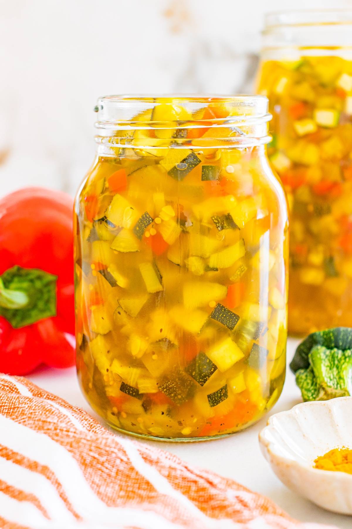 Jar filled with colorful homemade relish made of chopped vegetables, sitting on a table with fresh peppers.