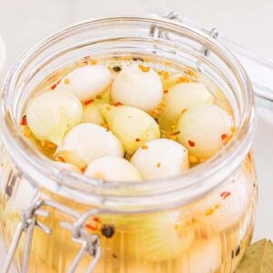 A glass jar of cocktail onions pickled with spices sits next to a container of salt and red pepper flakes.