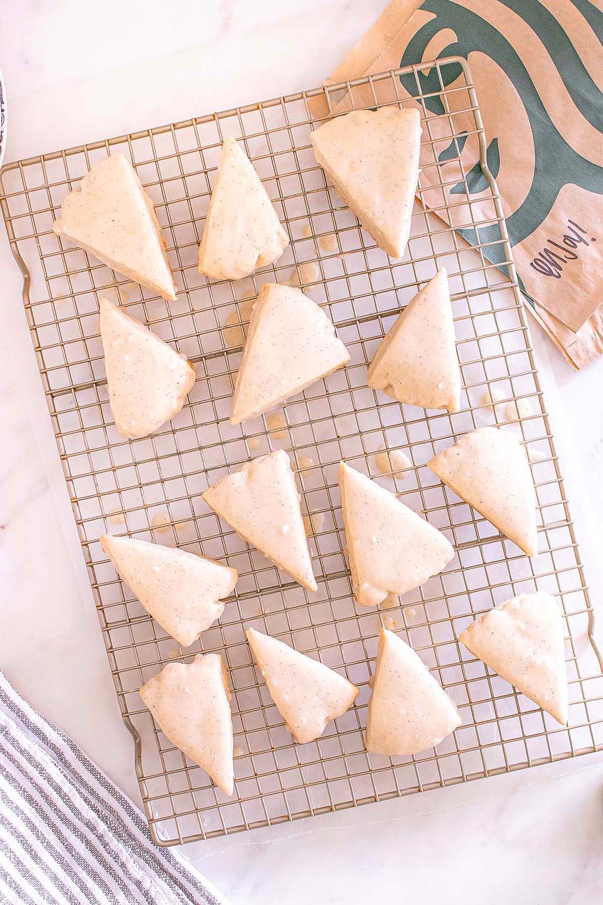 Fourteen Starbucks Copycat Vanilla Bean Scones cool on a wire rack, their shiny glaze tempting, with a Starbucks bag visible in the background.