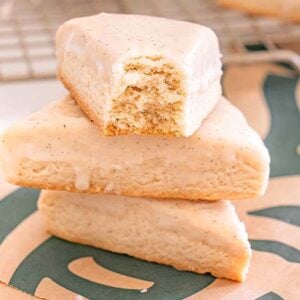 Three Starbucks Copycat Vanilla Bean Scones, one with a bite taken out, are stacked on a Starbucks napkin.