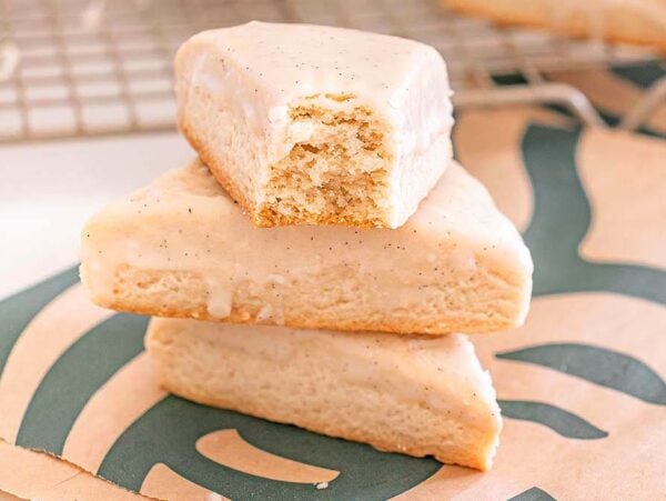 Three Starbucks Copycat Vanilla Bean Scones, one with a bite taken out, are stacked on a Starbucks napkin.