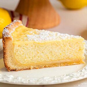 A slice of classic Italian rice pie, dusted with powdered sugar on a white plate, with lemons in the background.