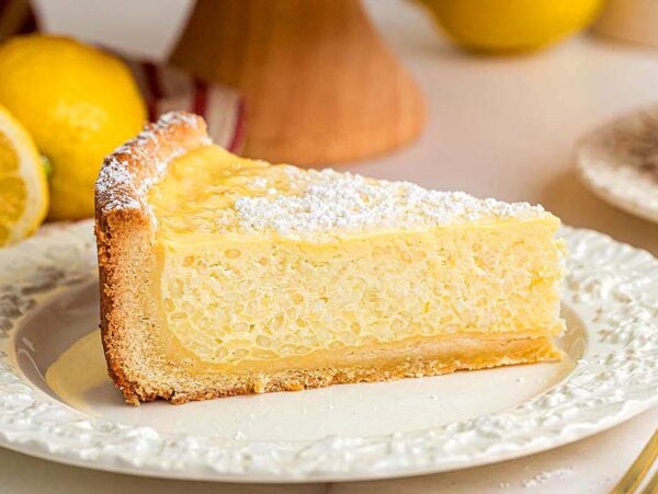 A slice of classic Italian rice pie, dusted with powdered sugar on a white plate, with lemons in the background.