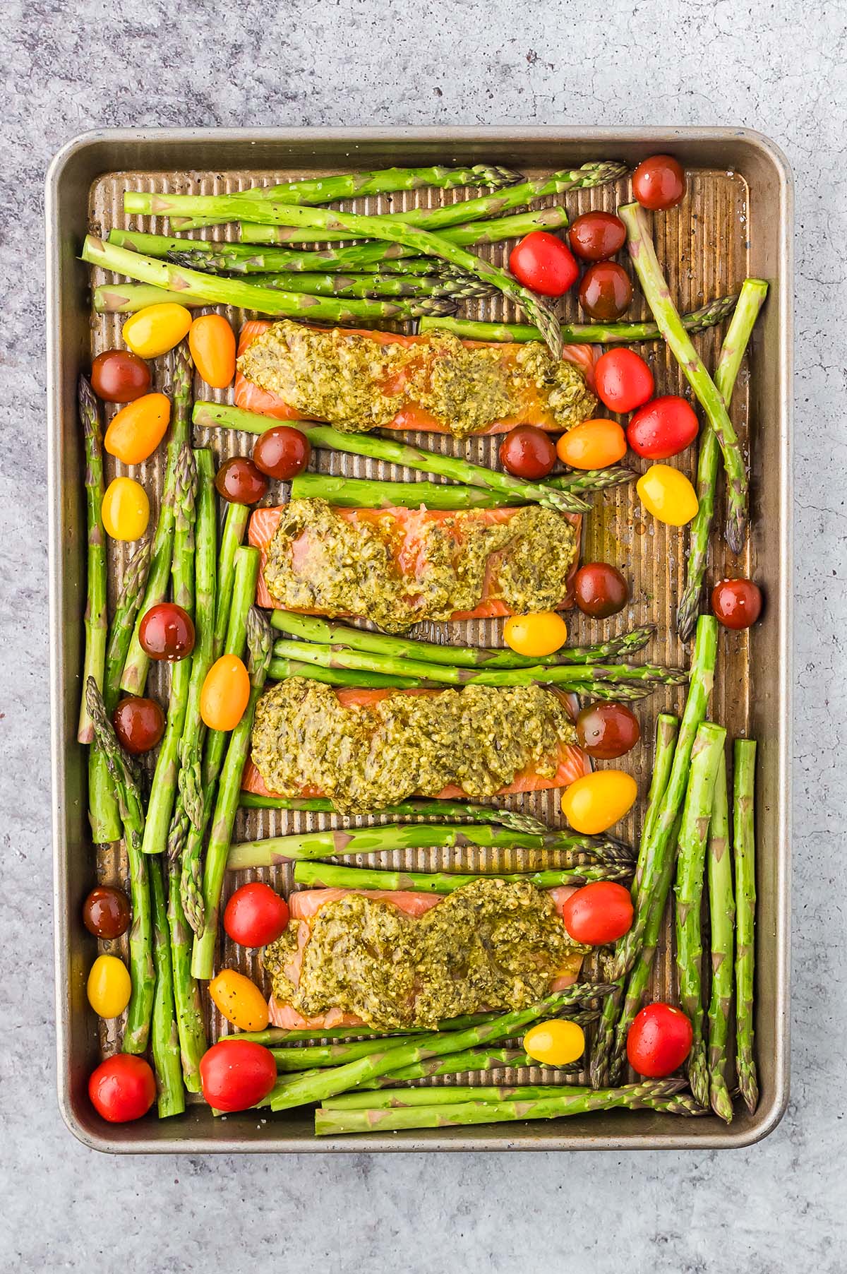 Sheet Pan Salmon and Asparagus with pesto, alongside vibrant red and yellow cherry tomatoes, ready for baking.