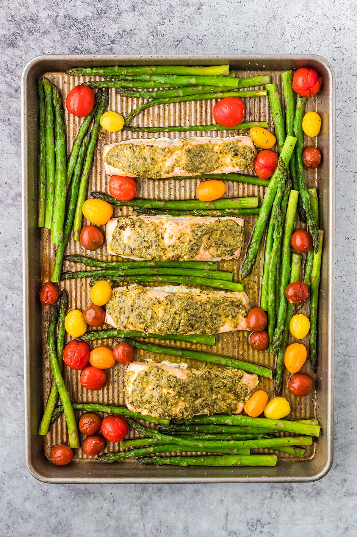 Enjoy Sheet Pan Salmon and Asparagus, featuring baked salmon fillets with pesto, tender asparagus, and vibrant cherry tomatoes—all roasted together for a simple yet delicious meal.