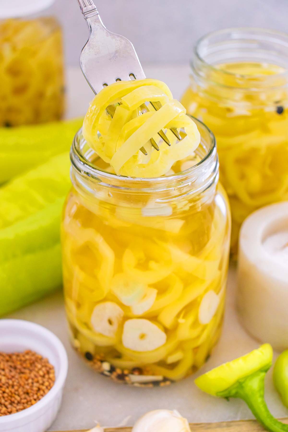 A fork lifts spiralized pickled yellow vegetables from a jar filled with pickled banana pickles, garlic, and spices.