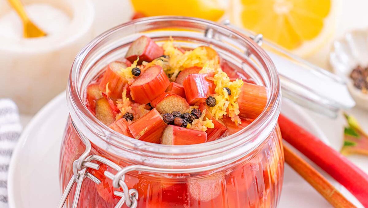 Glass jar filled with pickled rhubarb, lemon zest, and spices, with lemon slices and rhubarb stalks arranged nearby.