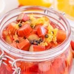 Glass jar filled with pickled rhubarb, lemon zest, and spices, with lemon slices and rhubarb stalks arranged nearby.