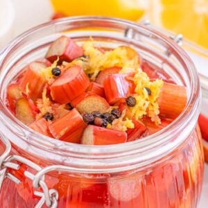 Glass jar filled with pickled rhubarb, lemon zest, and spices, with lemon slices and rhubarb stalks arranged nearby.