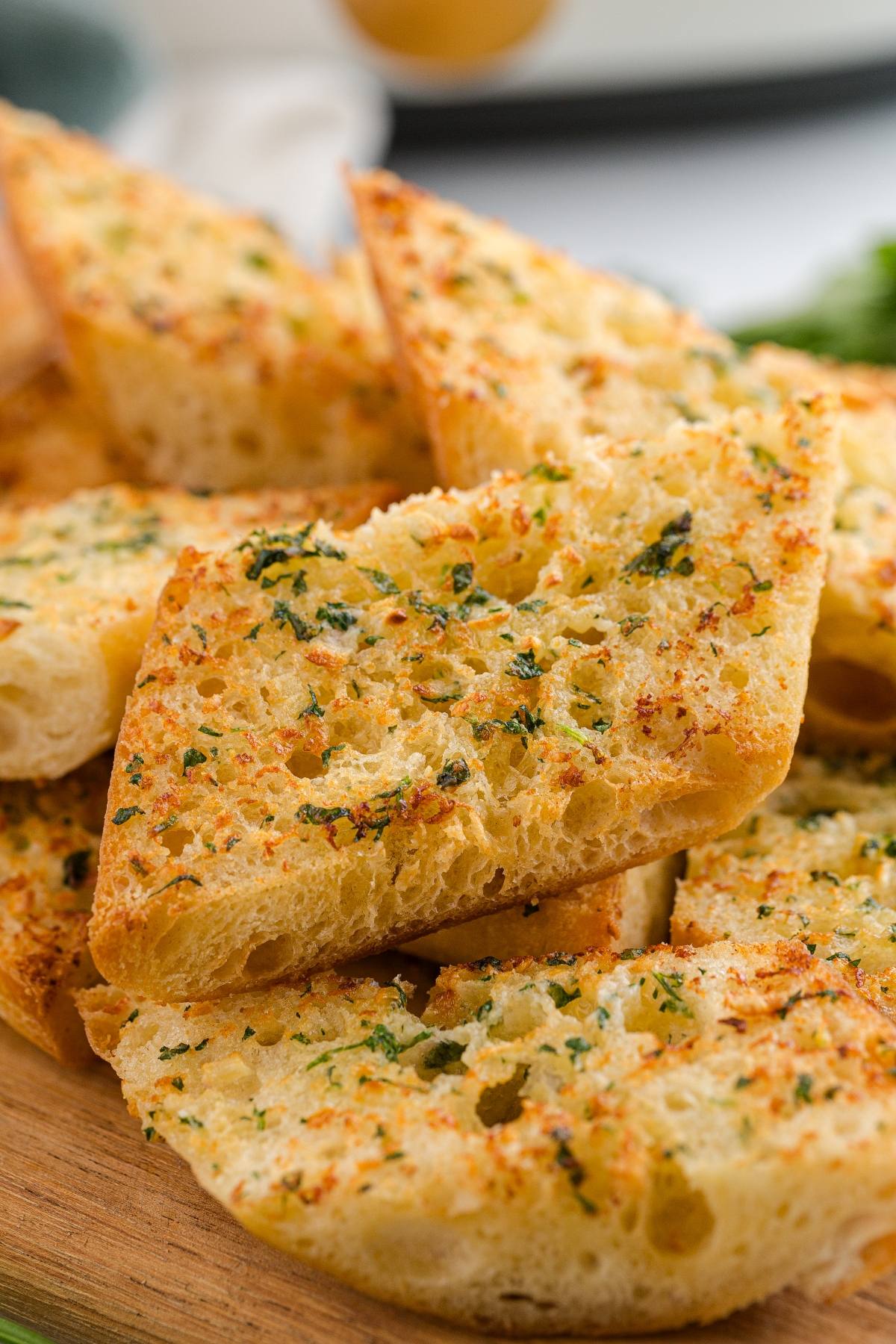 Slices of garlic bread topped with herbs and seasoning, stacked on a wooden surface.