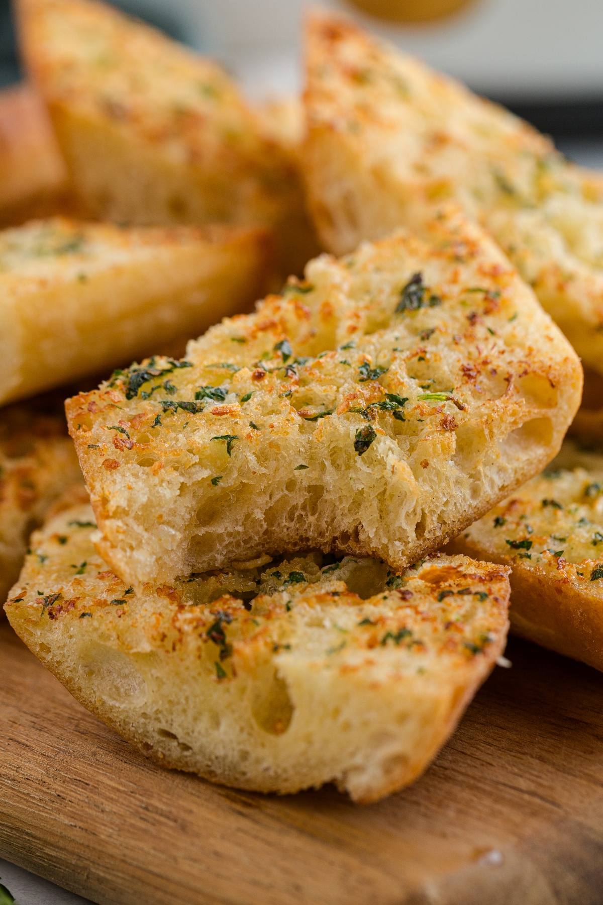 Sliced garlic bread with herbs stacked on a wooden board.