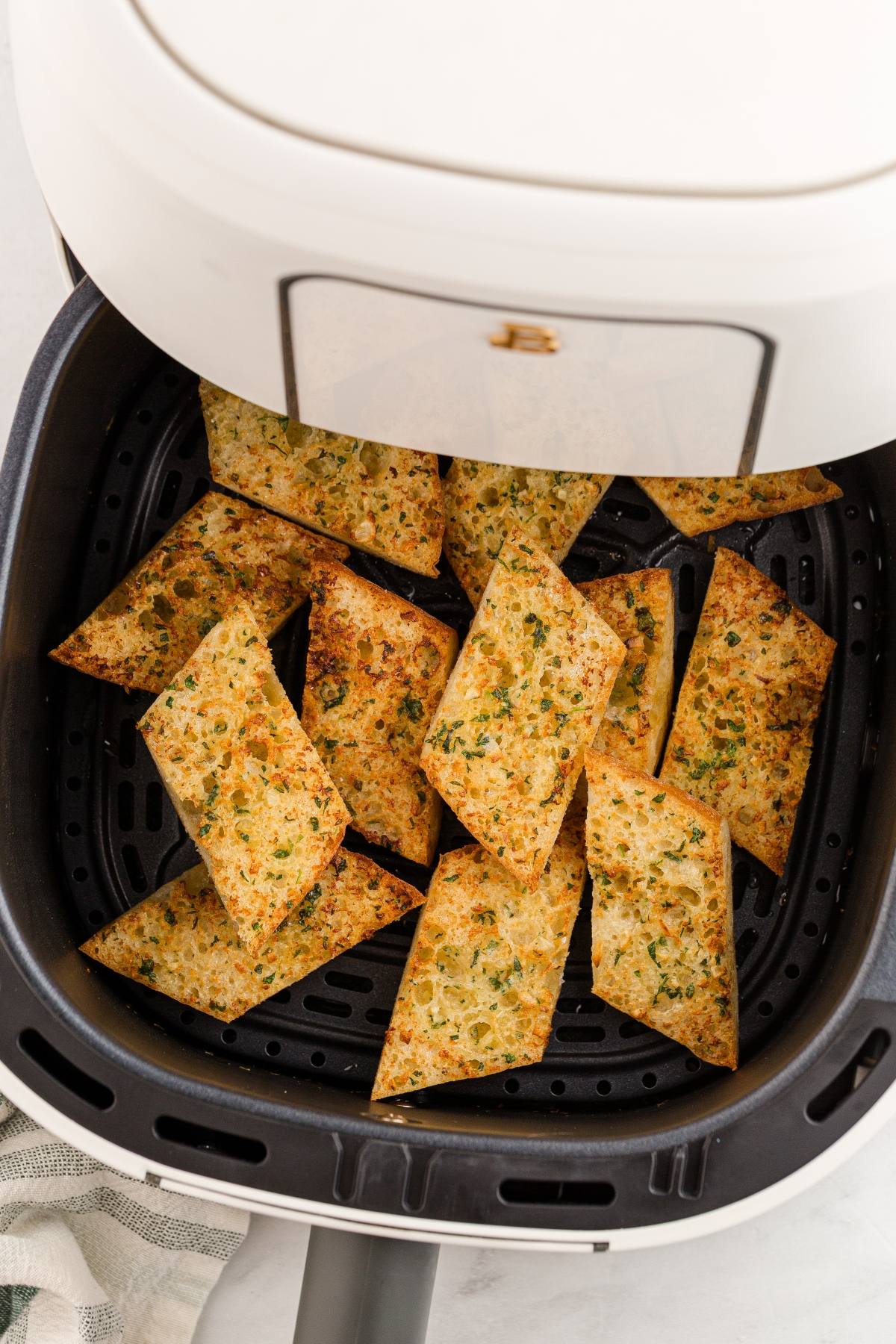 Air fryer basket with golden, crispy garlic bread pieces arranged neatly inside.