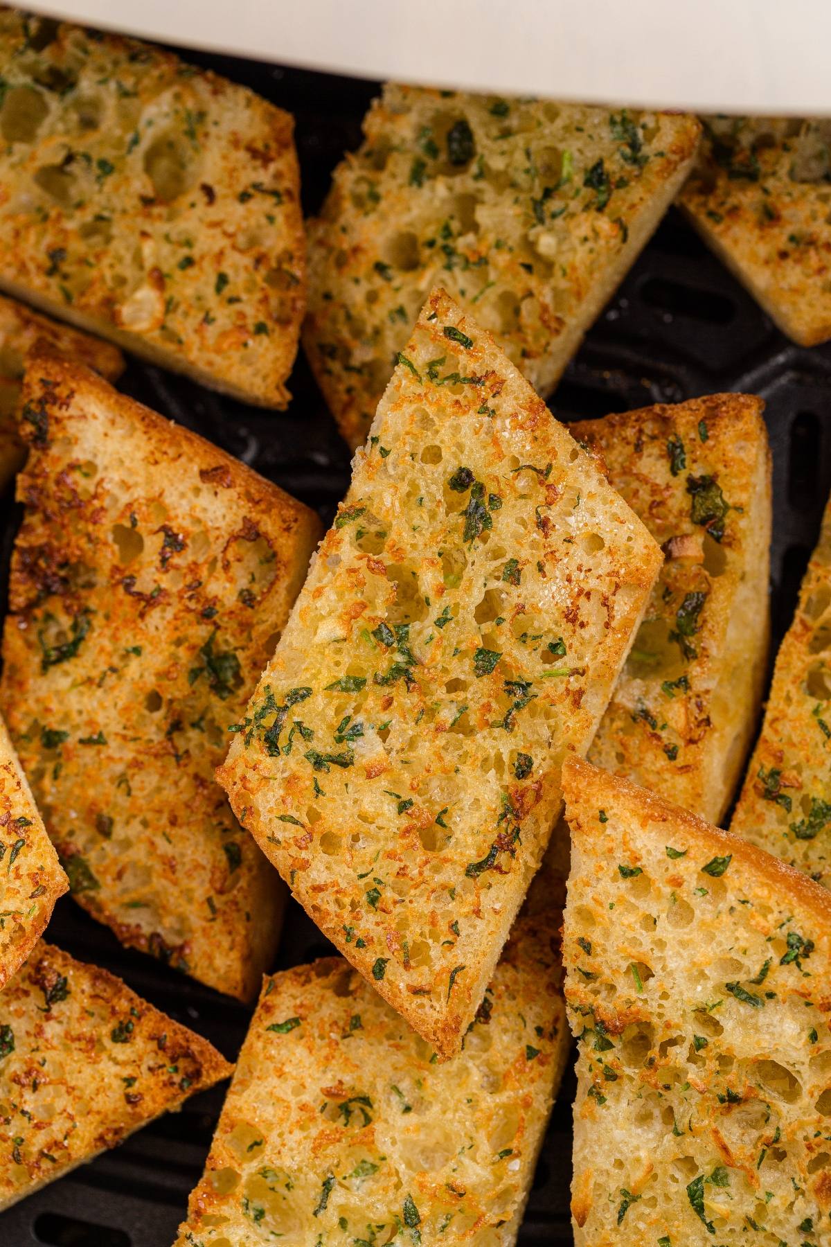 Slices of golden, crispy garlic bread topped with herbs, arranged closely together.