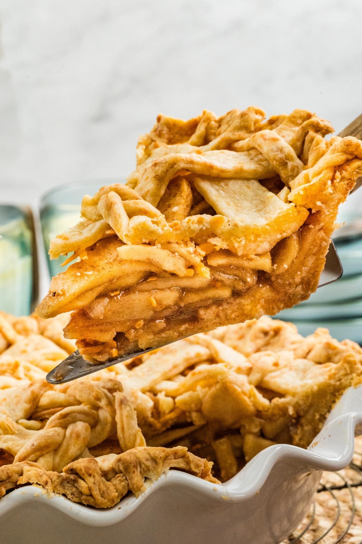 A close-up of a slice of apple pie with a golden, flaky lattice crust being lifted from a pie dish.