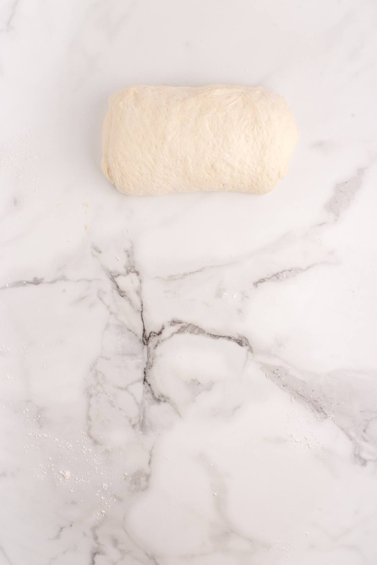 A ball of dough sits on a white marble surface.