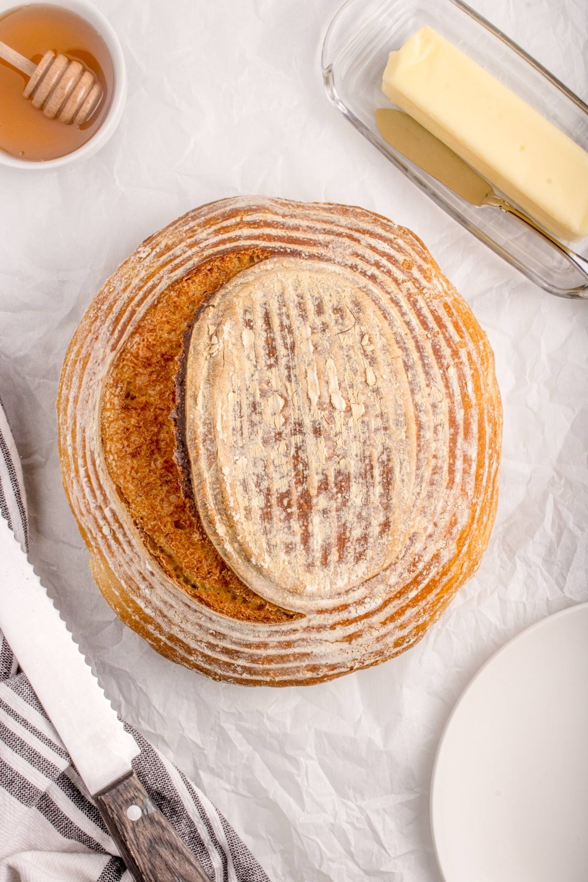 Two round loaves of artisan bread on parchment with butter, honey, a knife, and a plate nearby.