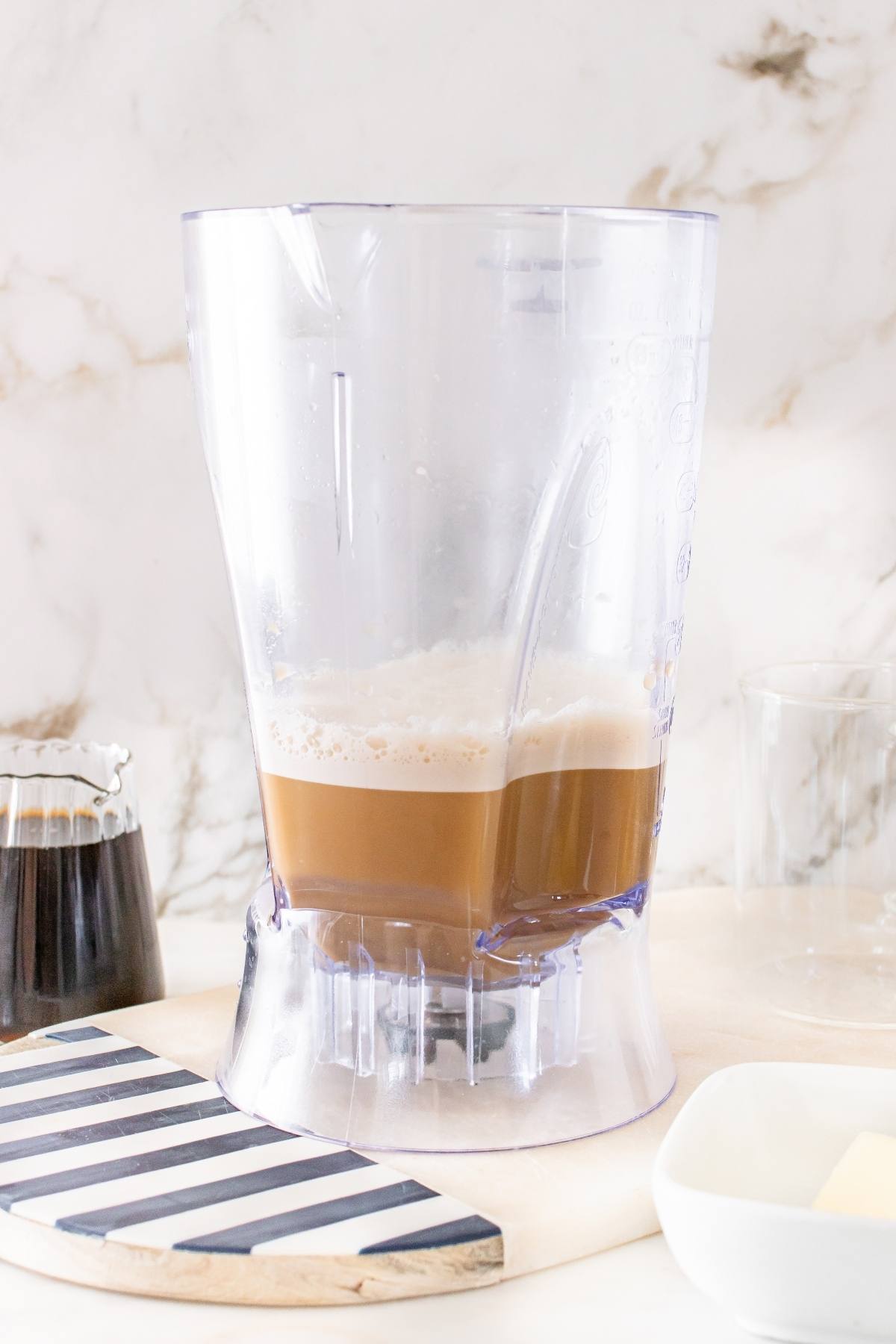 A blender pitcher filled with blended coffee on a kitchen counter with coffee and utensils nearby.