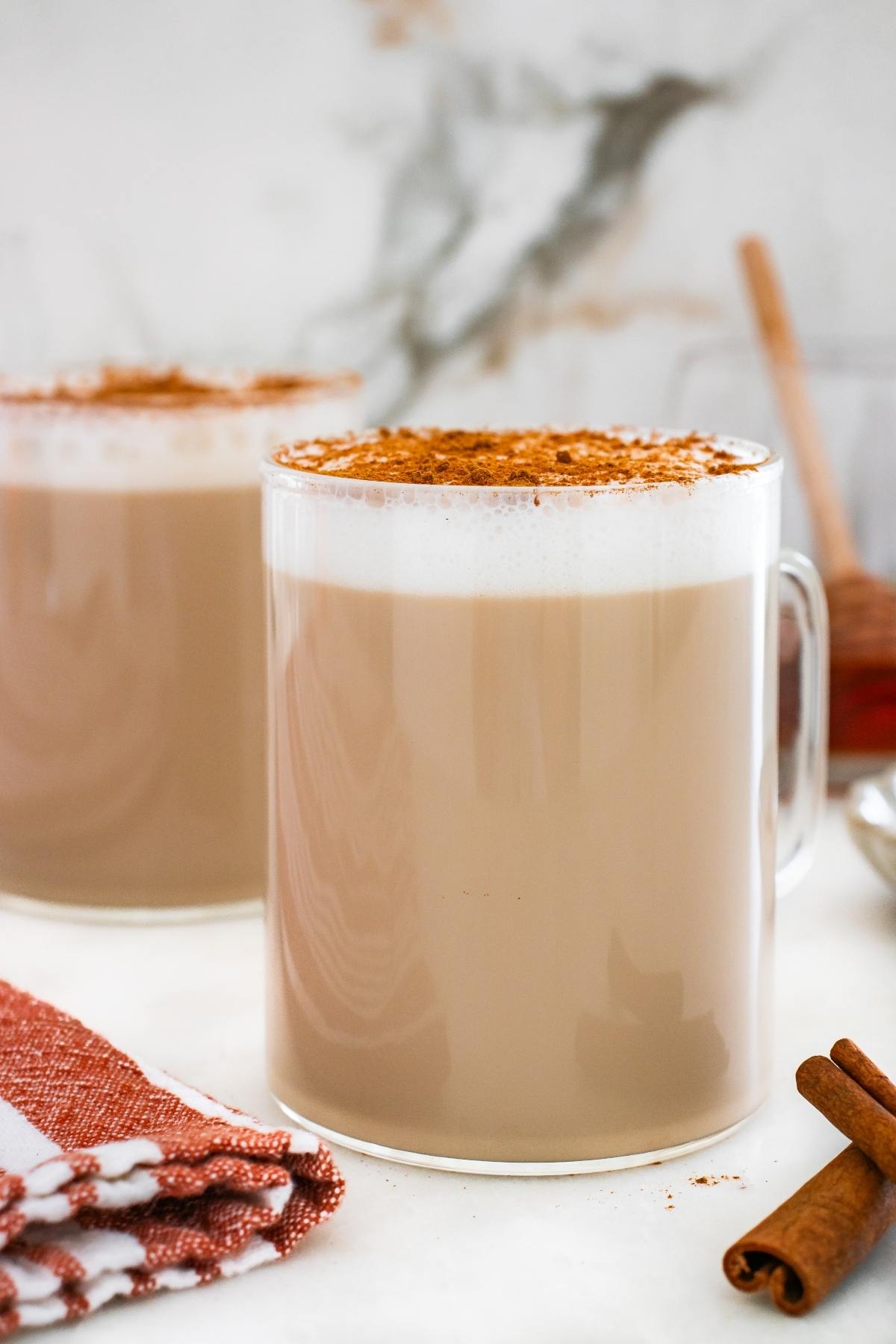 A glass mug of chai latte topped with cinnamon, next to a napkin and cinnamon sticks.