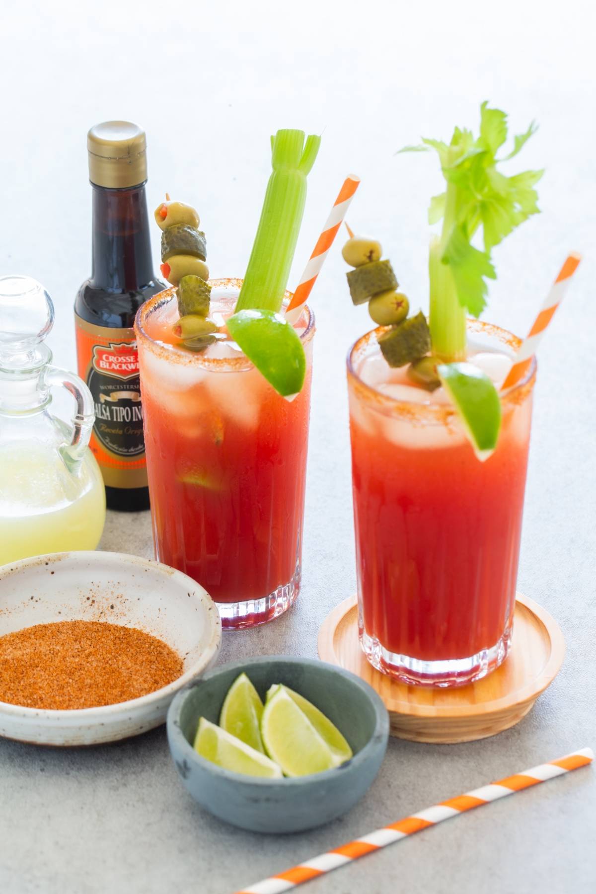 Two Bloody Mary cocktails with celery, olives, and limes, surrounded by caesar cocktail ingredients—seasonings, lime wedges, and sauces—celebrate Canada's National Drink in style.