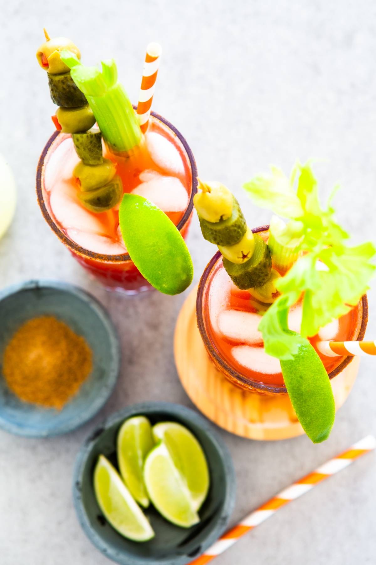 Two Bloody Mary cocktails with ice, celery, pickles, lime wedges, and striped straws, seen from above—a perfect cocktail for Canada Day.