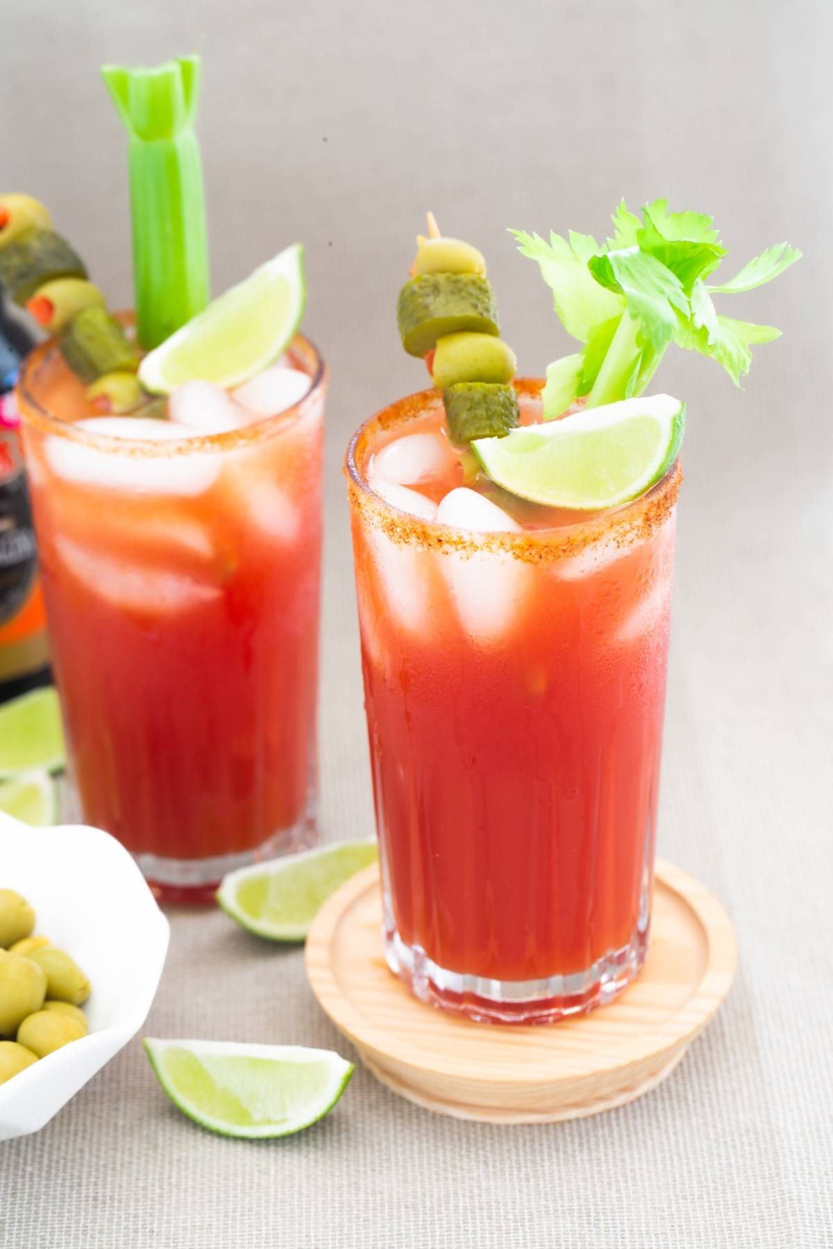 Two Bloody Mary cocktails—often called Canada’s National Drink when made with caesar cocktail ingredients like Clamato juice—are garnished with celery, lime, and olives, served over ice in tall glasses.