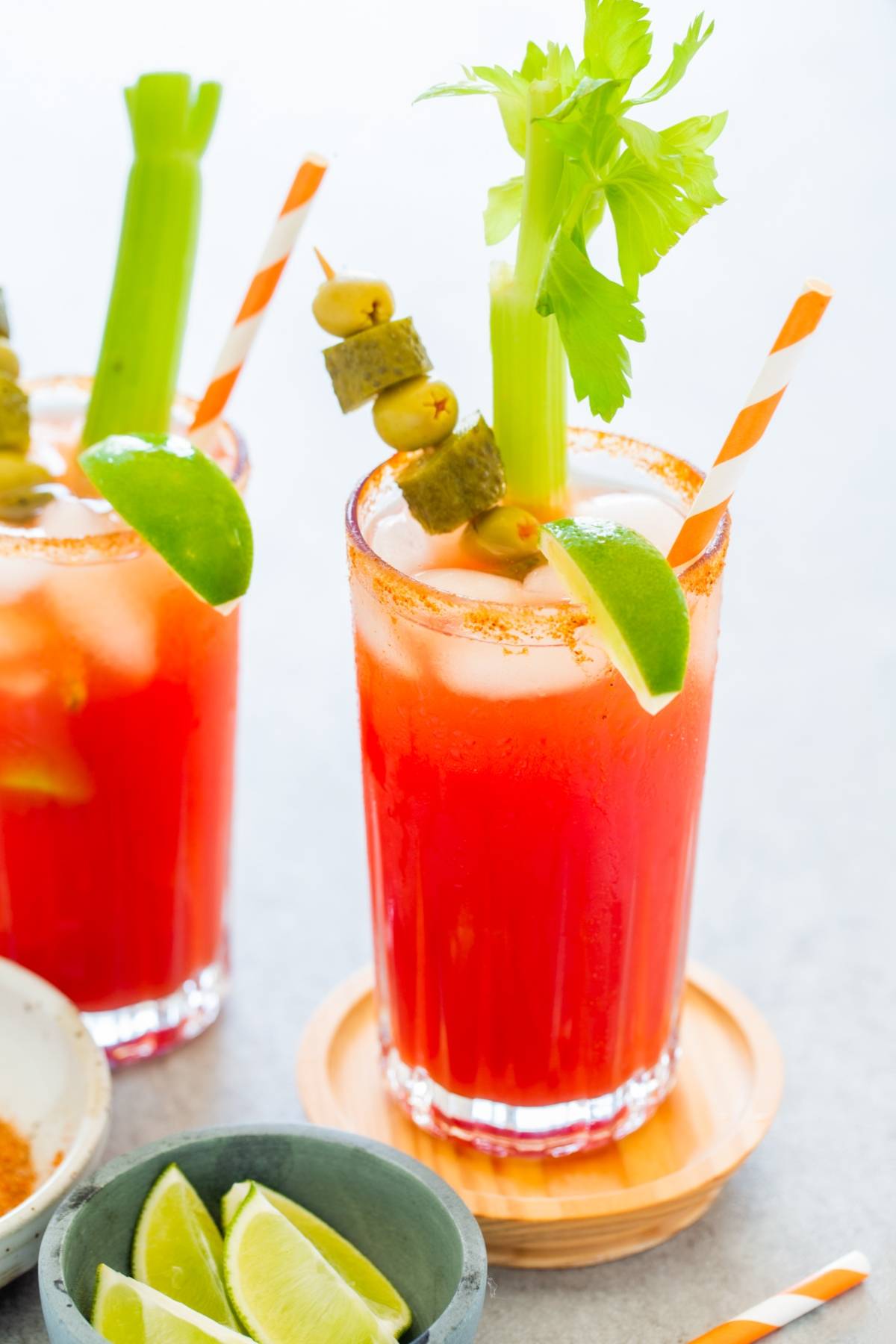 Two Canadian Caesar Cocktails—Canada's National Drink—garnished with celery, olives, pickles, lime wedges, and striped straws. This twist on a Bloody Mary with Clamato juice is perfect for brunch or any festive gathering.