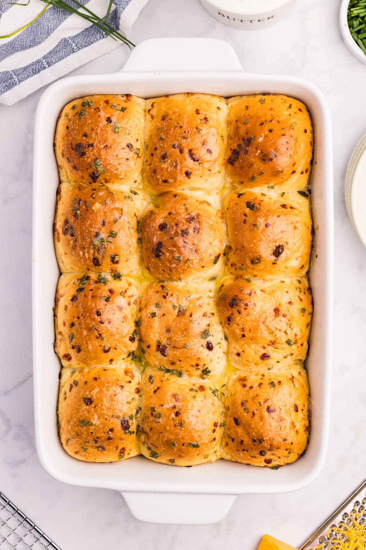 Golden, herbed dinner rolls in a white baking dish on a marble countertop.