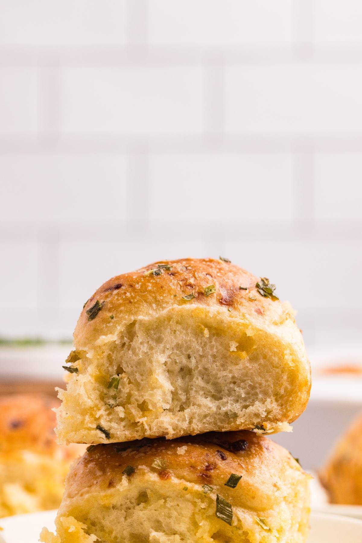 Two fluffy, golden brown bread rolls with herbs stacked on top of each other against a tiled background.