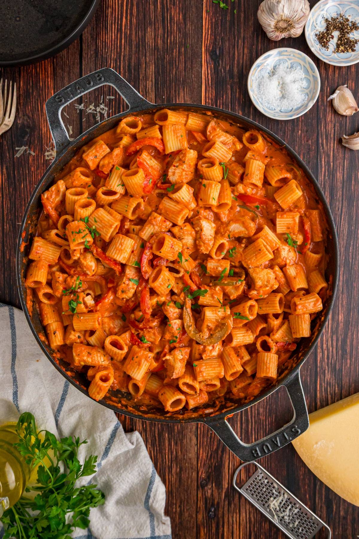 A skillet filled with creamy rigatoni pasta, chicken, and red peppers on a rustic wooden table.