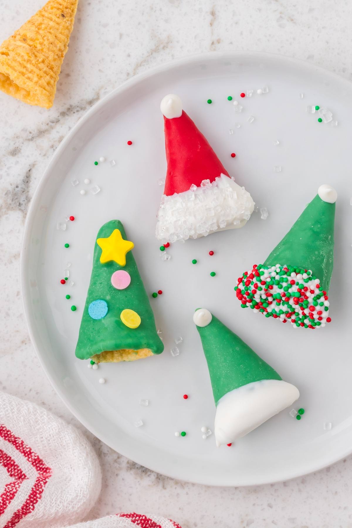 Four festive Christmas treats shaped like Santa hats and trees, decorated with colorful icing and sprinkles.
