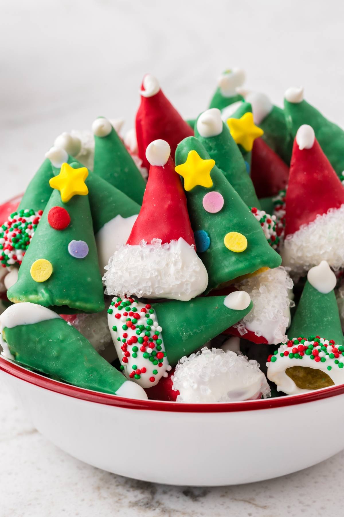 Bowl of colorful Christmas cookies decorated as Santa hats and trees with icing and sprinkles.