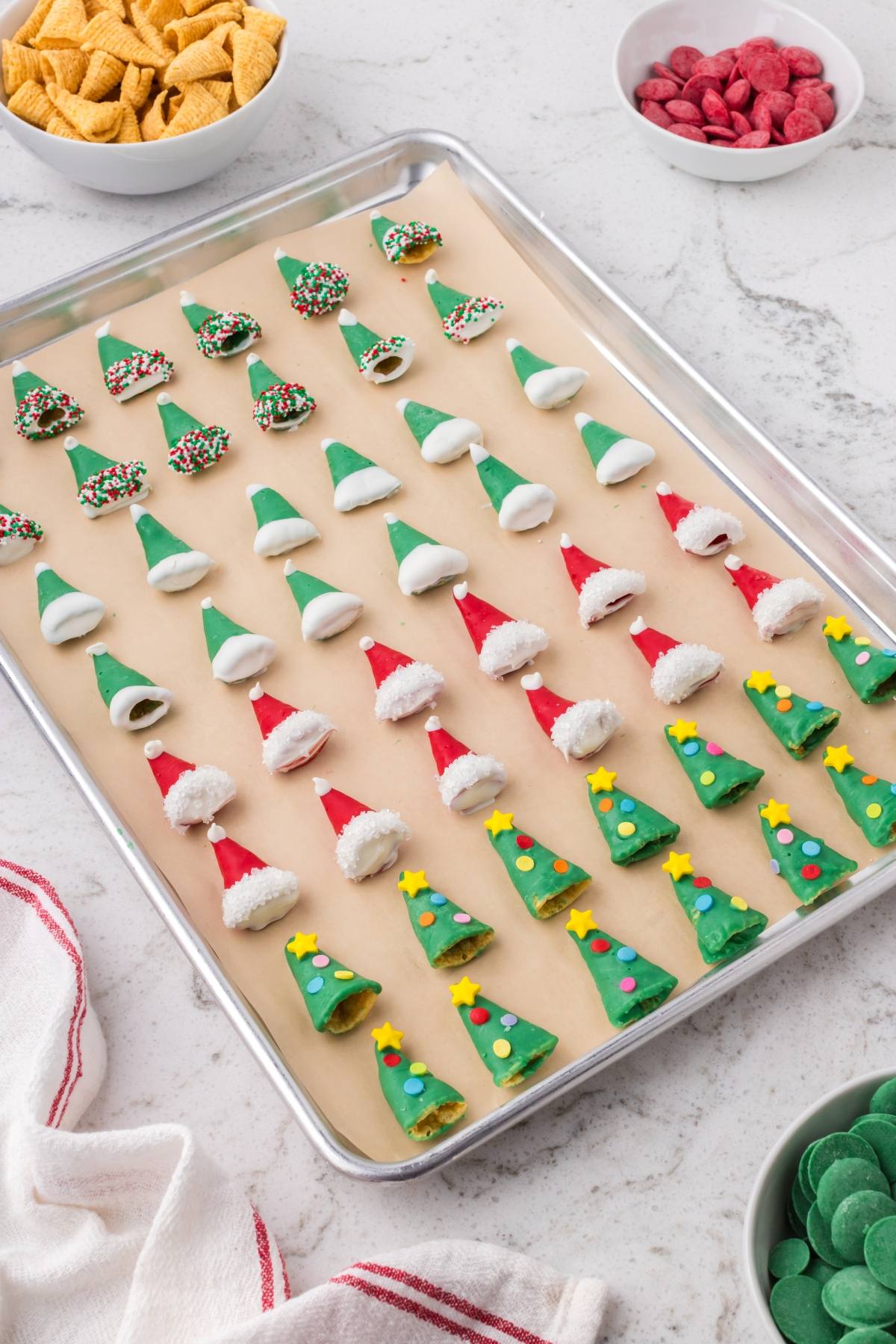 A tray of Christmas-themed treats shaped like trees, hats, and other holiday shapes, decorated with colorful candies.