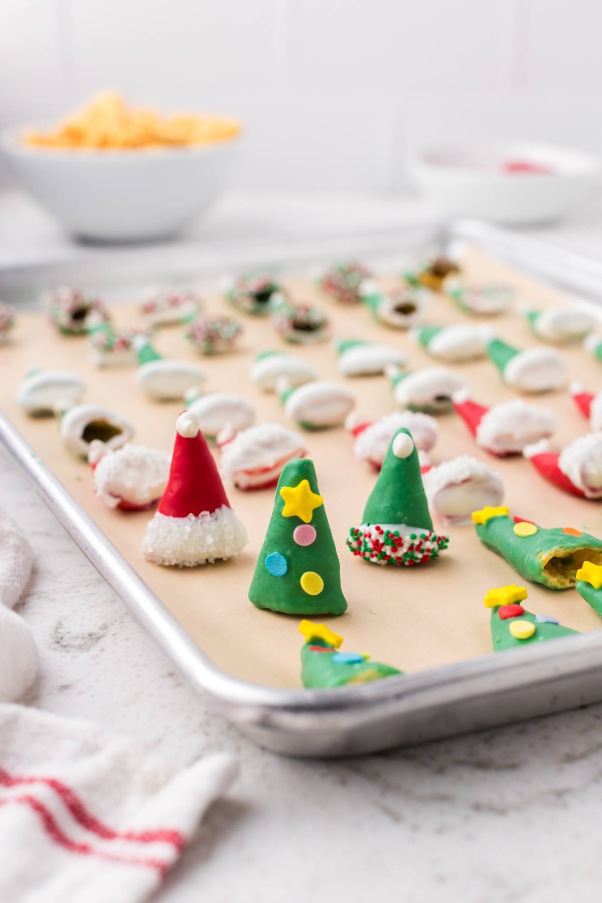 Colorful Christmas tree and Santa hat treats on a baking sheet, decorated with icing and sprinkles.