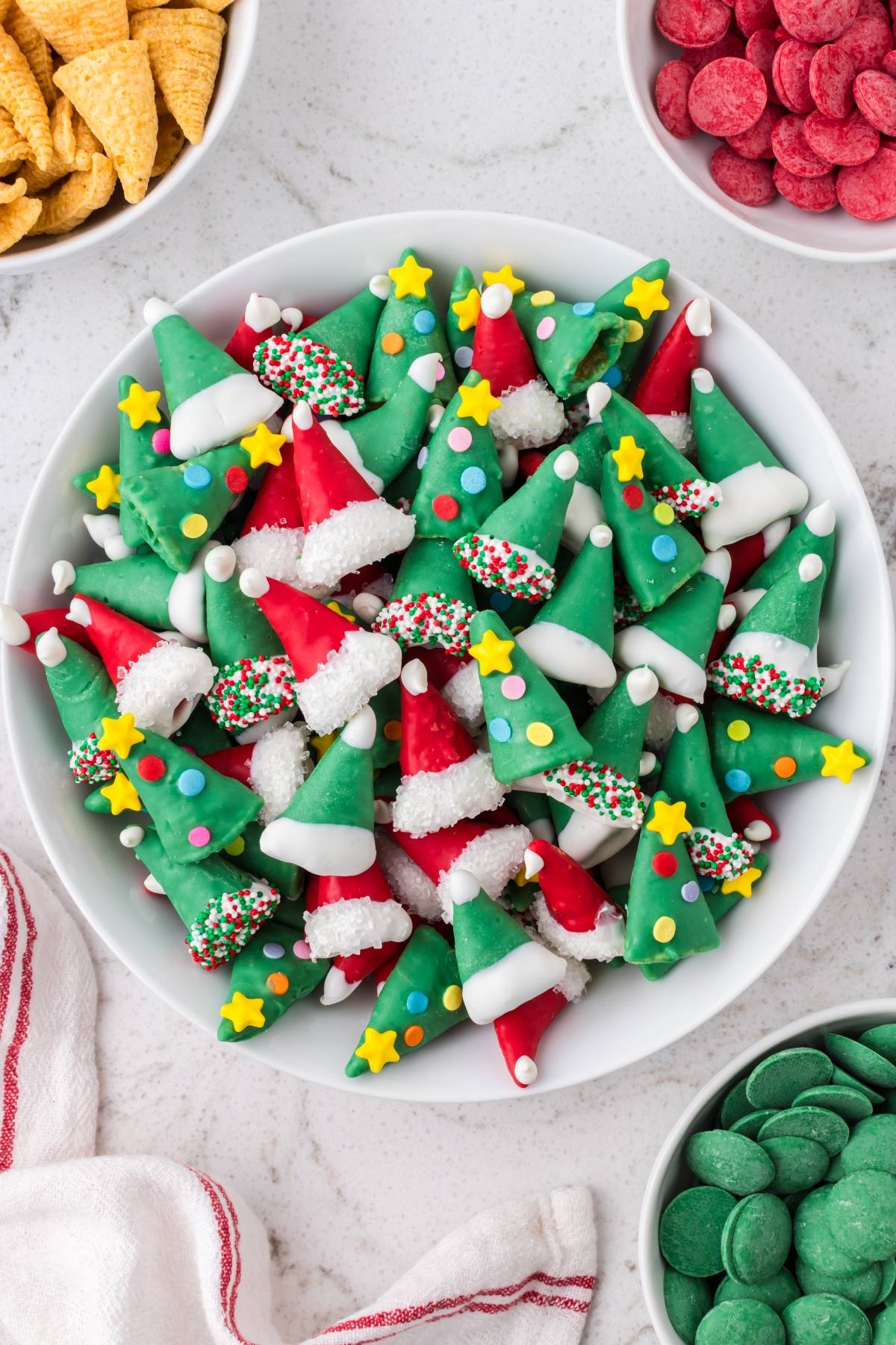 Plate of festive Christmas tree-shaped candies with green and red colors, sprinkles, and star decorations.