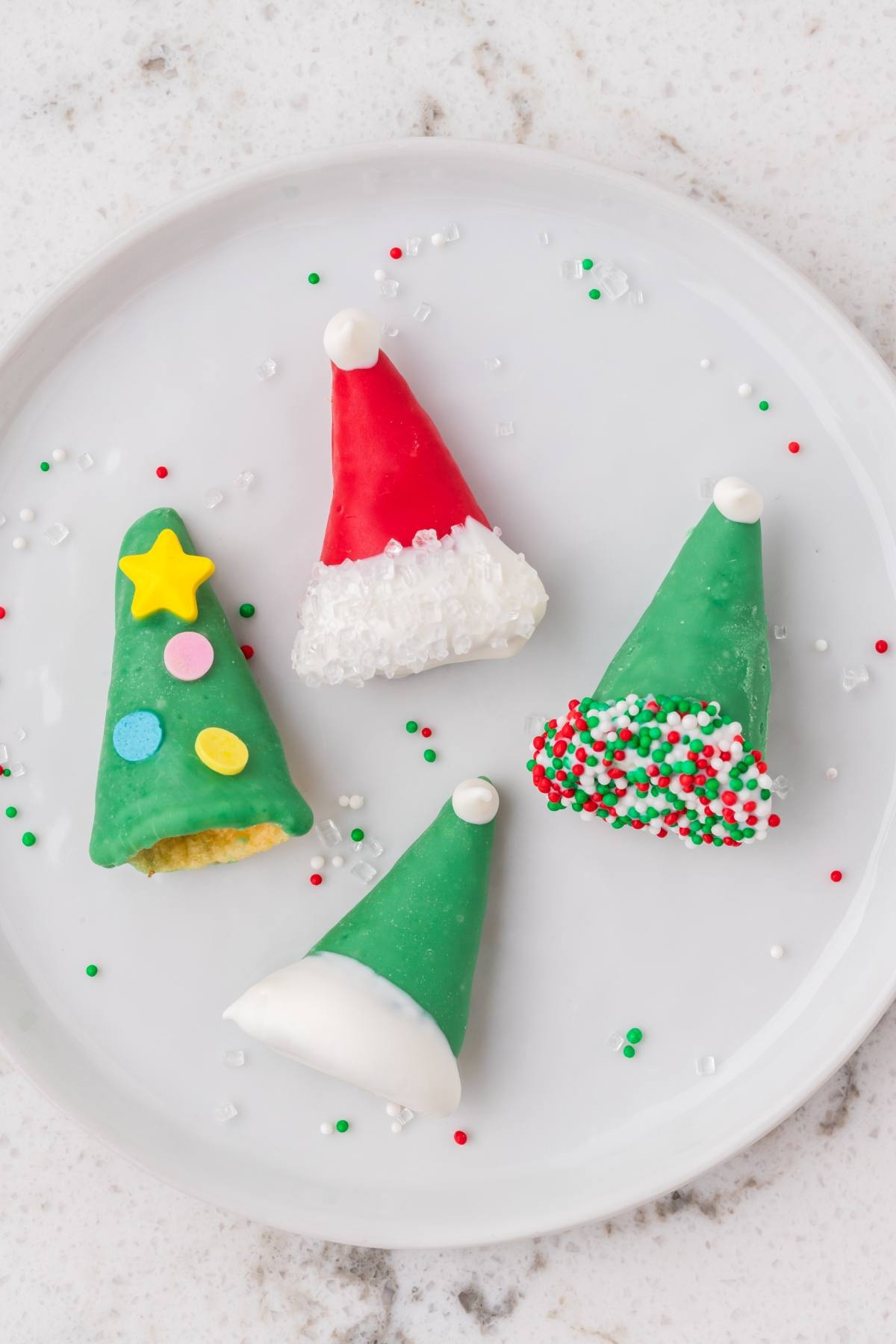 Four festive Christmas-themed treats decorated as Santa hats and Christmas trees on a white plate.