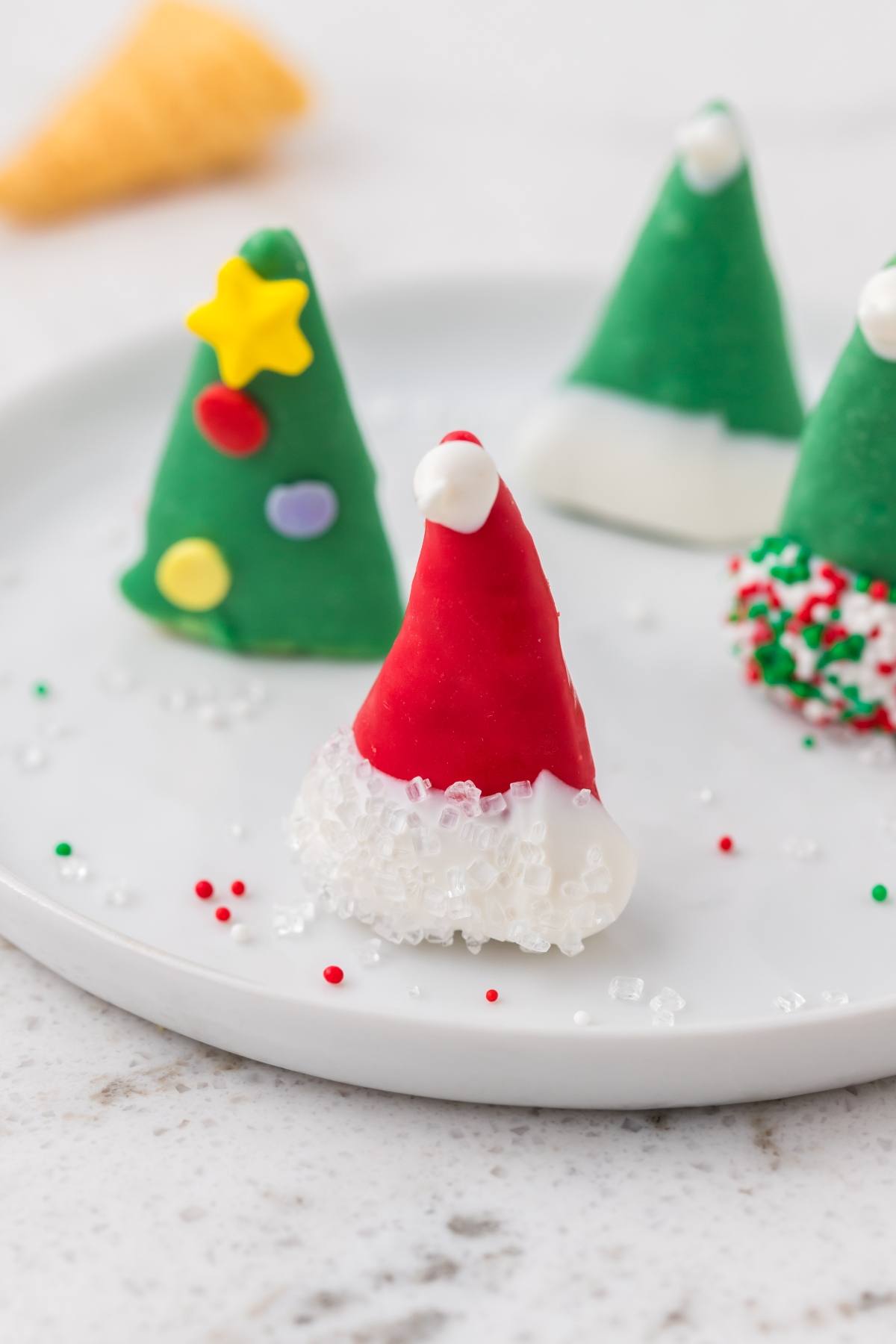 A plate with Christmas tree and Santa hat-shaped holiday treats decorated with icing and sprinkles.