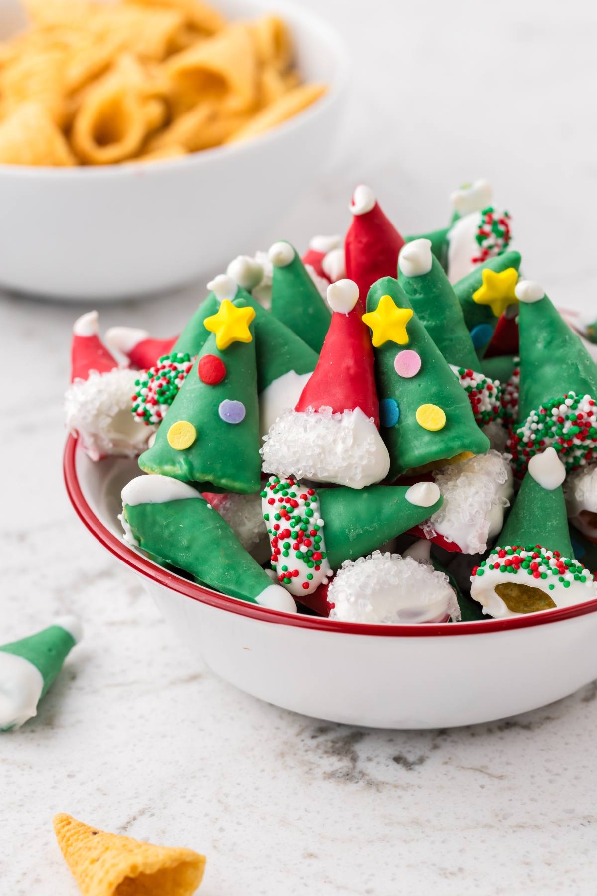 A bowl of corn chips decorated as festive Christmas trees and Santa hats with colorful icing and sprinkles.