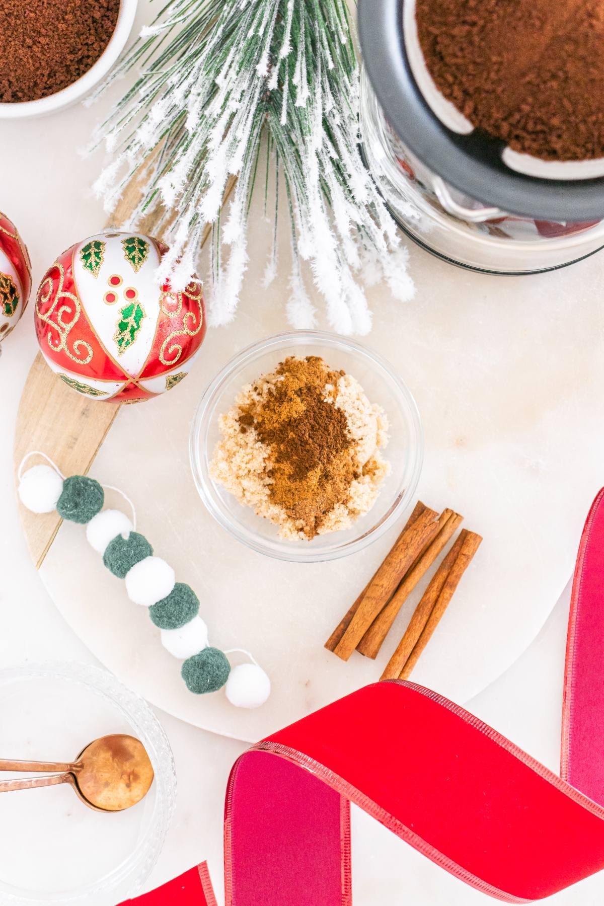 A bowl of oatmeal with cinnamon, cinnamon sticks, ornaments, and a red ribbon on a white surface.