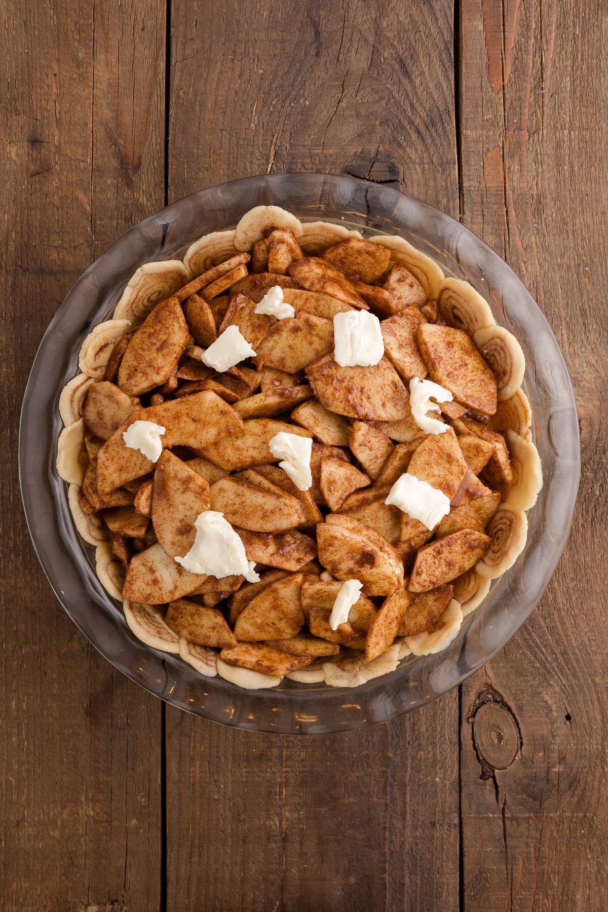 Unbaked apple pie with cinnamon apple slices and butter in a pie crust on a rustic wooden table.