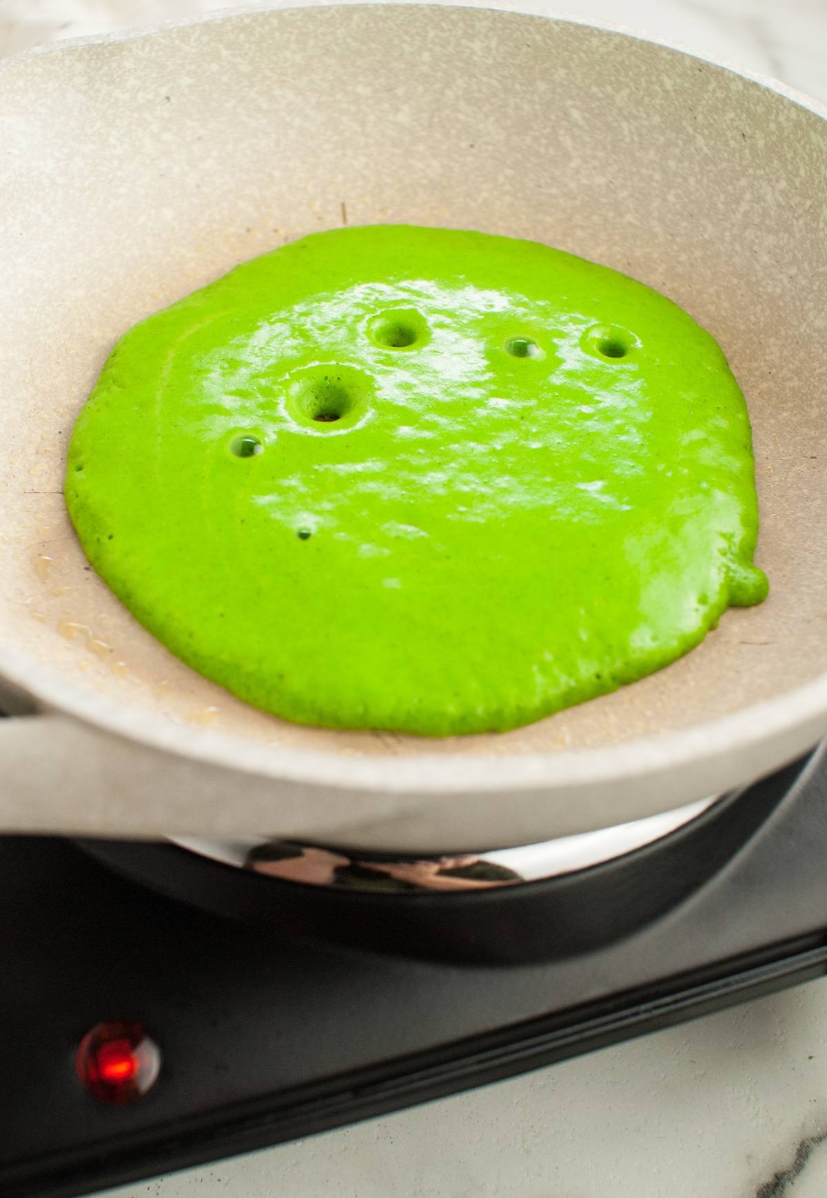 Bright green pancake batter cooking in a pan, with bubbles forming on the surface—perfect for spooky breakfast ideas or Halloween recipes for kids.