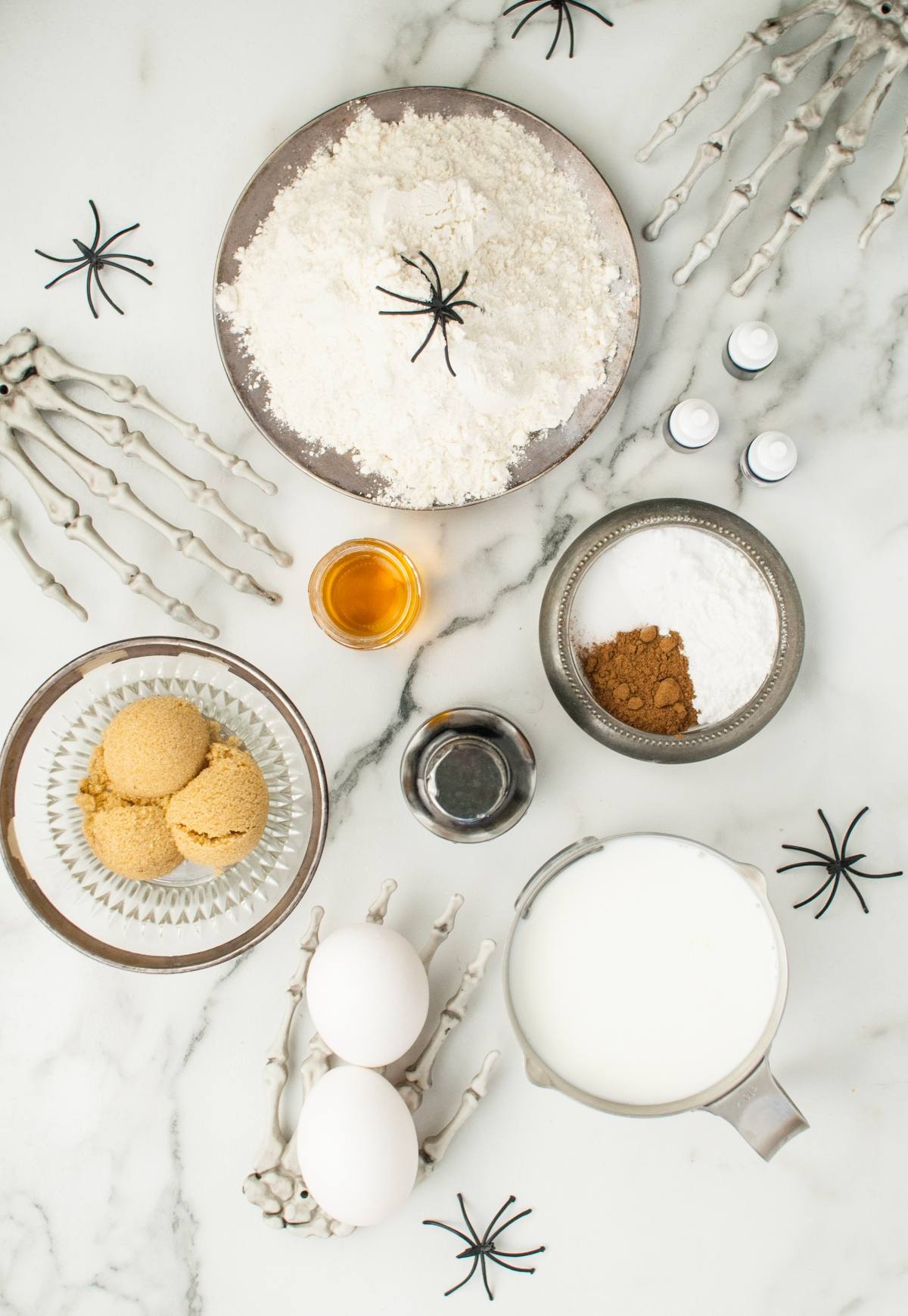 Baking ingredients on a marble counter with fake spiders and skeleton hands set the stage for spooky breakfast ideas and Halloween recipes for kids.