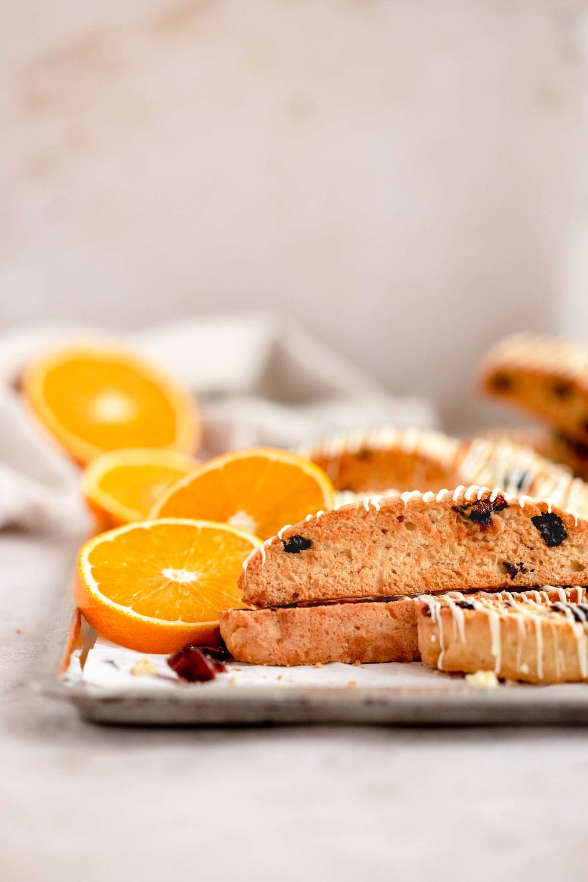 Cranberry orange biscotti with dried fruit and white drizzle, served alongside fresh orange slices on a tray.