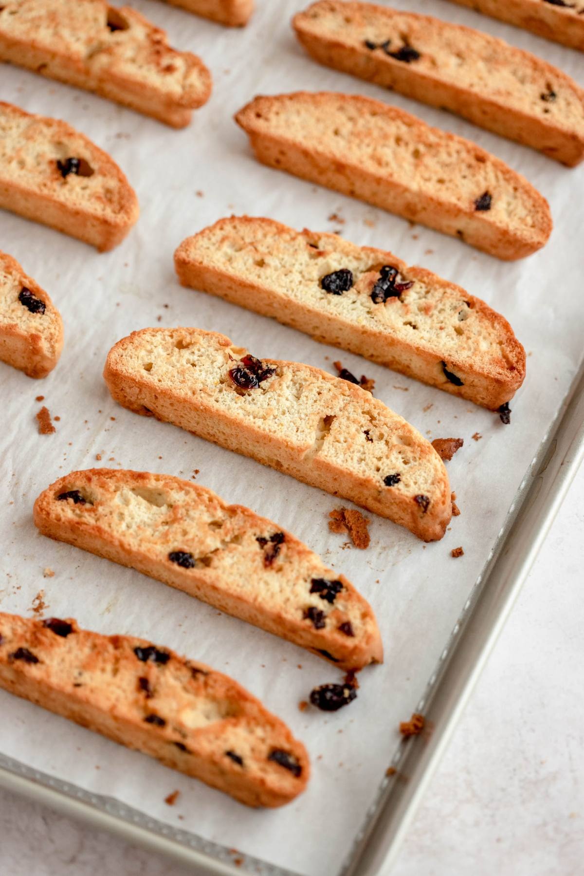 Crispy cranberry orange biscotti cookies with dried fruit on a baking sheet lined with parchment paper.