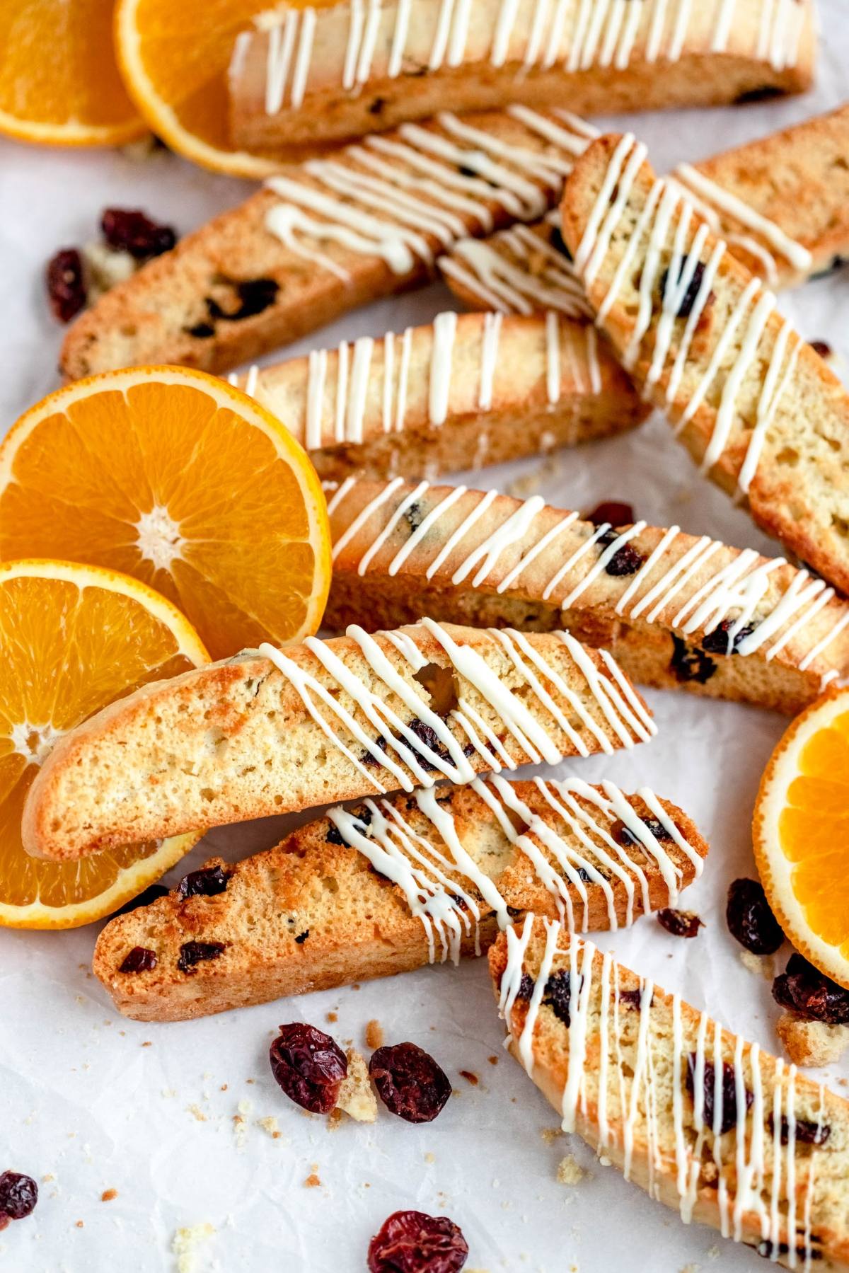 Cranberry orange biscotti drizzled with white icing, topped with dried cranberries and orange slices, displayed on a white surface.