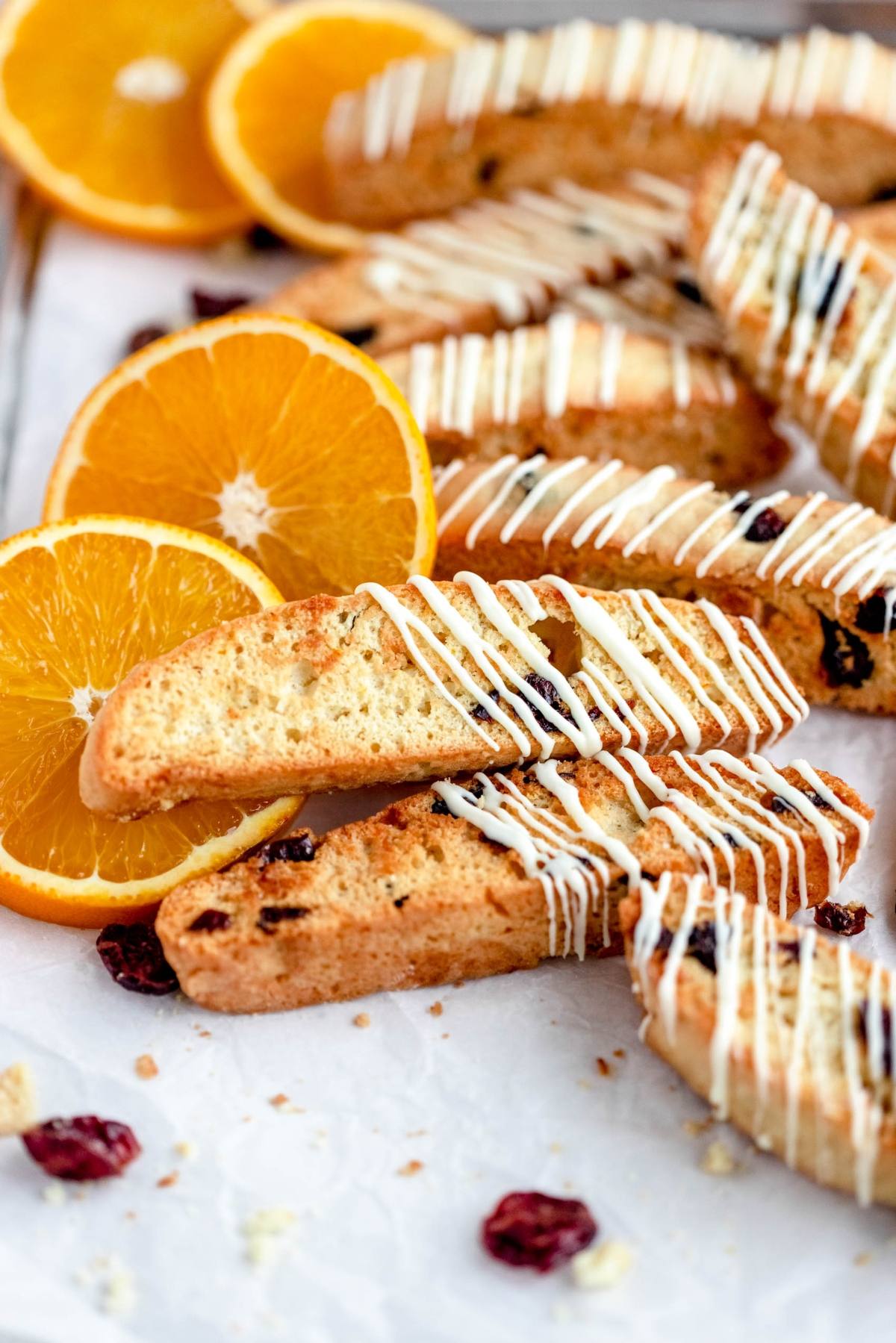 Cranberry orange biscotti with white icing, topped with dried cranberries and orange slices, arranged on a white surface.