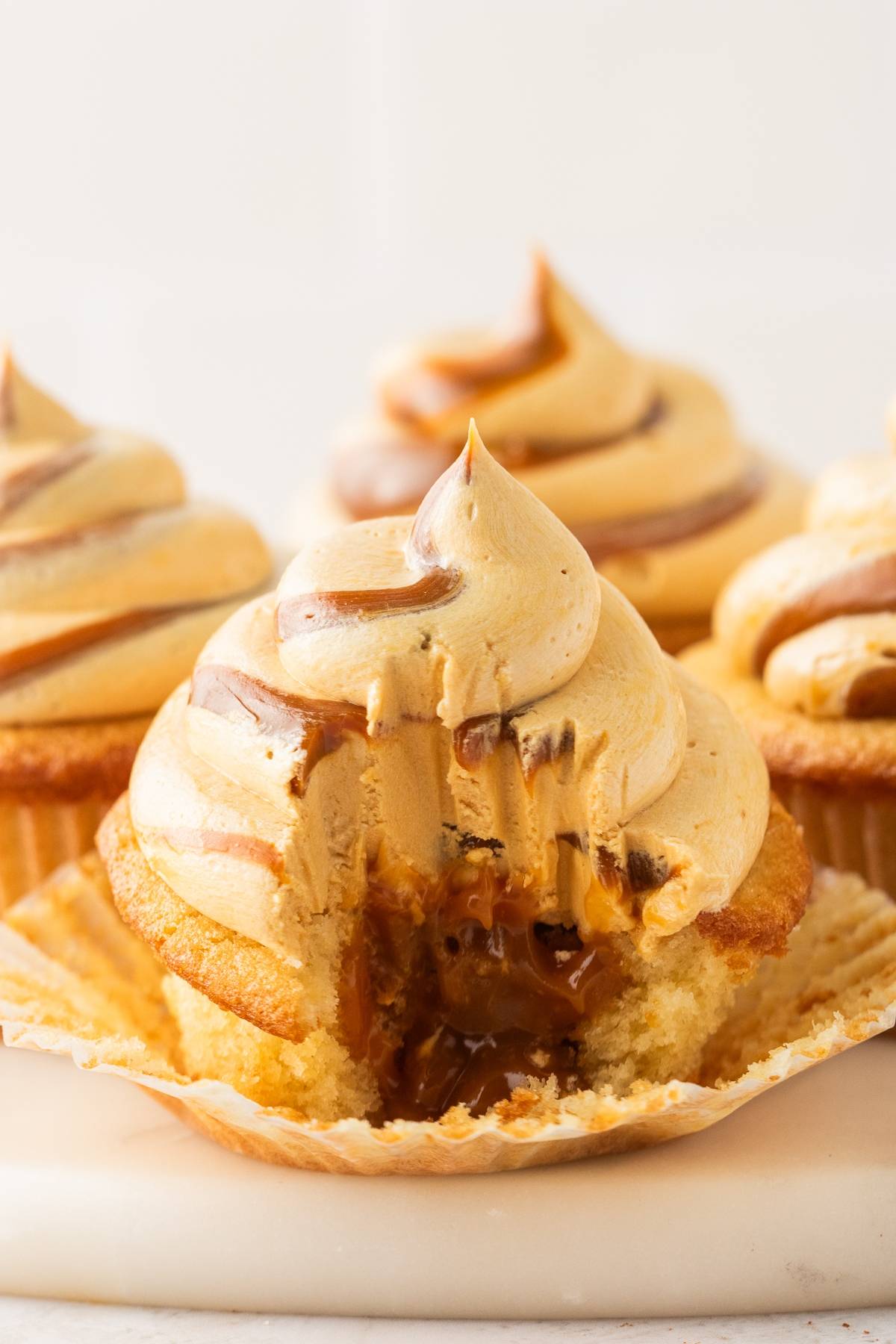 A caramel-filled cupcake with swirled frosting, one bite taken, sitting on a paper liner.