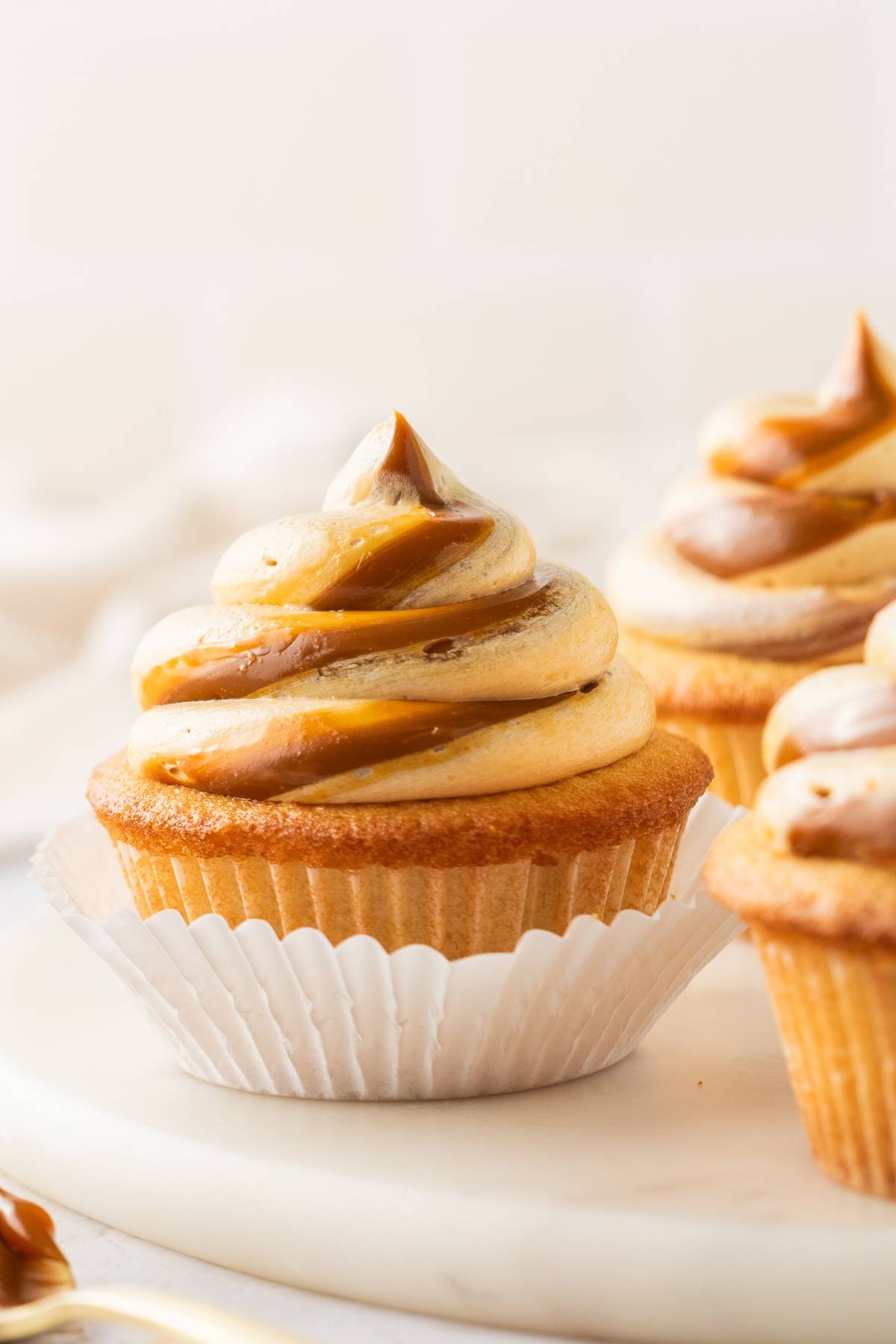 Vanilla cupcake with swirled caramel frosting, unwrapped and sitting on a white surface.