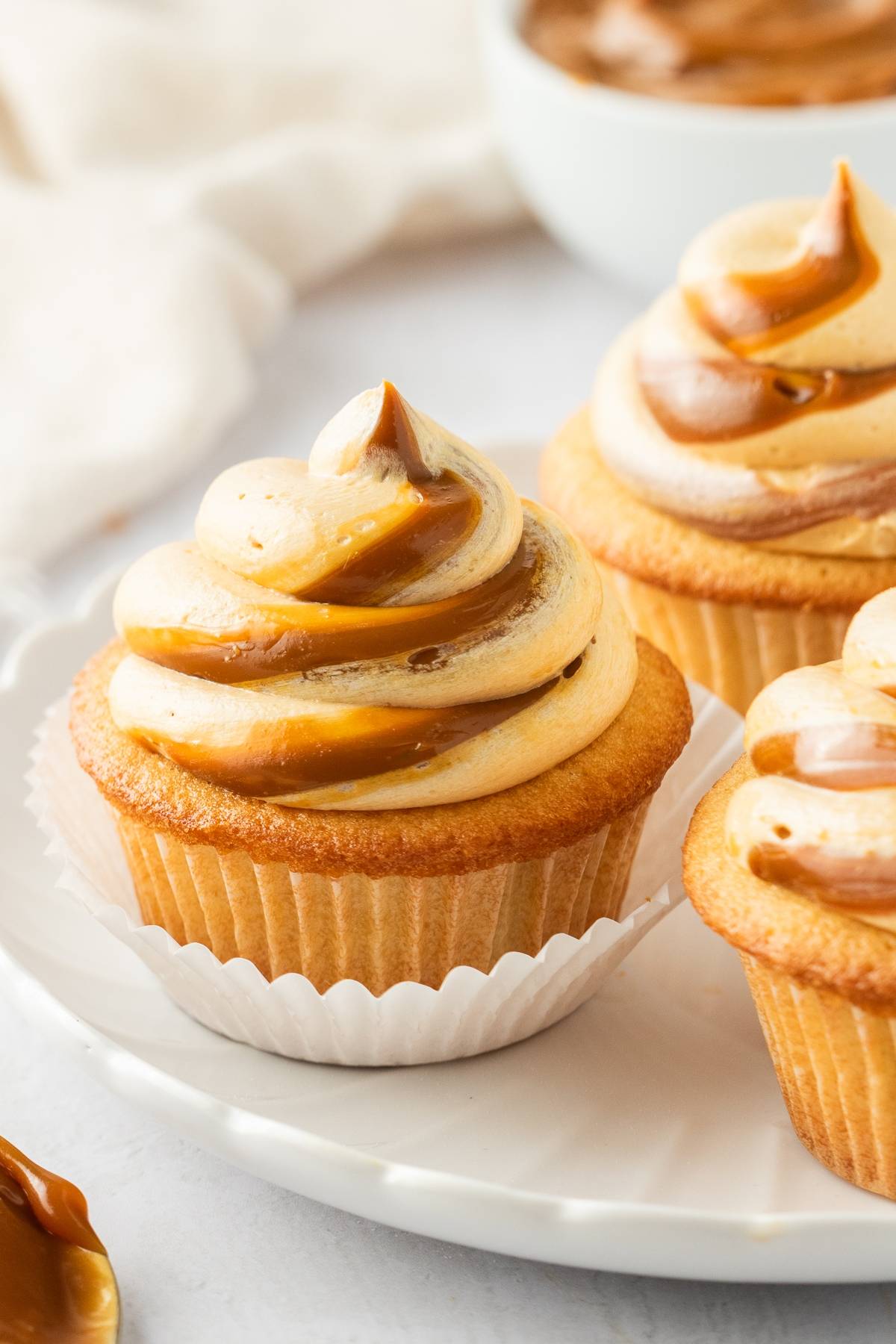 Vanilla cupcakes with swirled caramel and vanilla frosting on a white plate.