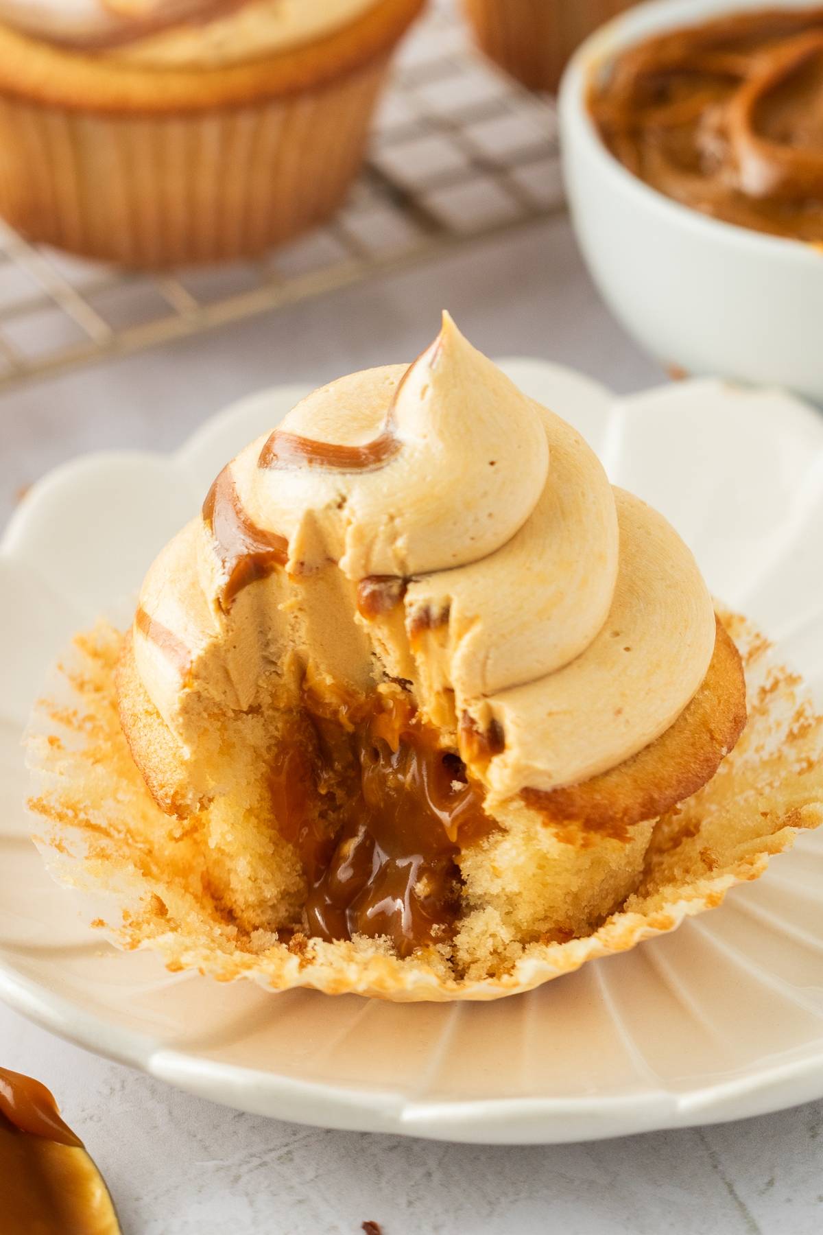 Cupcake with caramel filling and swirled frosting, partially eaten, on a white plate.